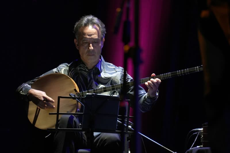 Murat Aydemir playing the tanbur on a concert stage