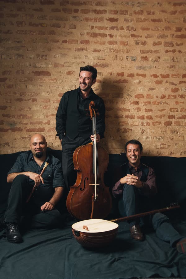 The trio seated with their instruments against a brick wall
